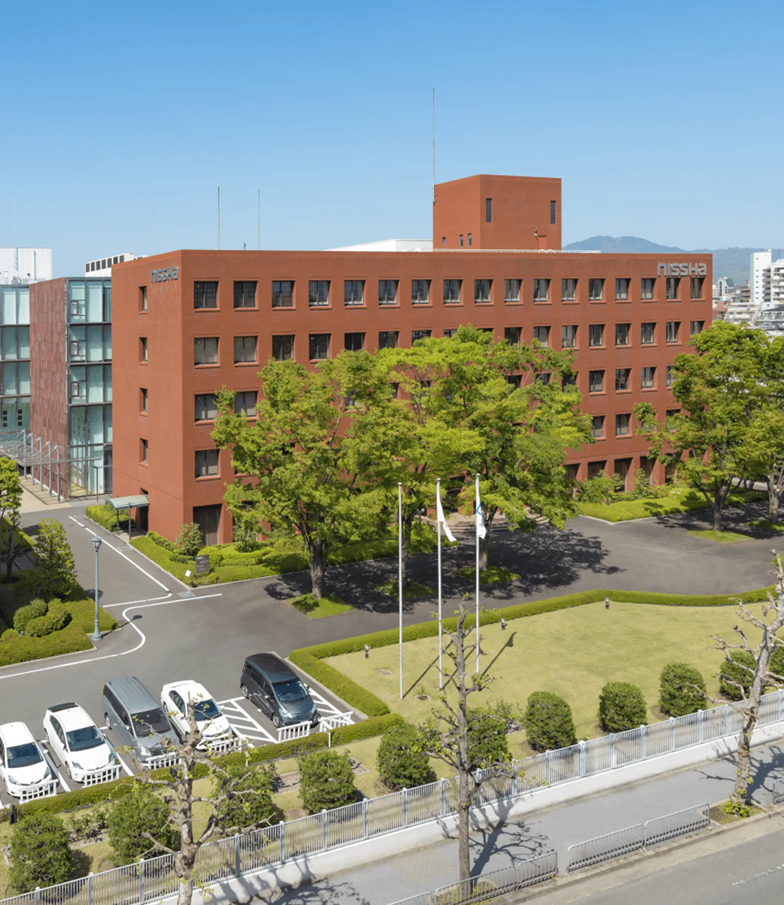 Nissha headquarters building surrounded by trees and parking area under a clear blue sky, representing the company’s commitment to innovation and sustainability.