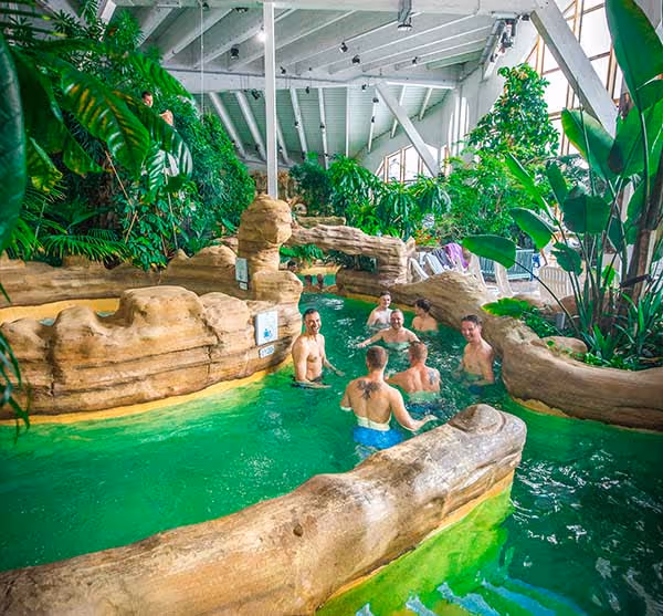 People having fun in the indoor swimming pool, with jungle decoration and green water