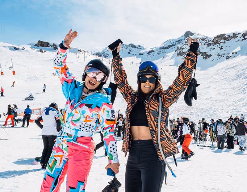 Two girls wearing retro ski clothing against snowy mountain backdrop
