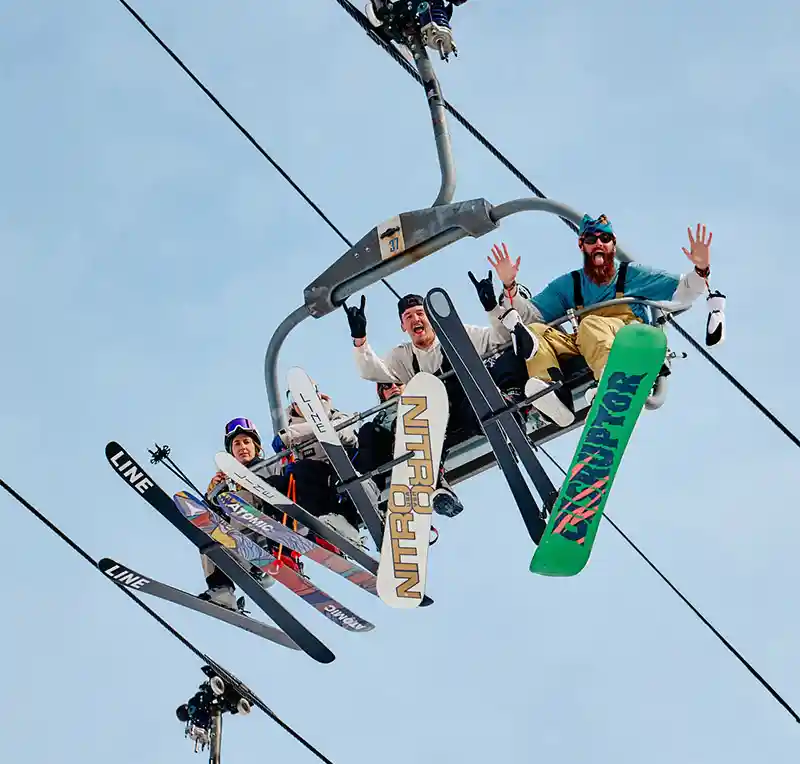 A group of people looking down from a ski lift making faces at the camera in excitement