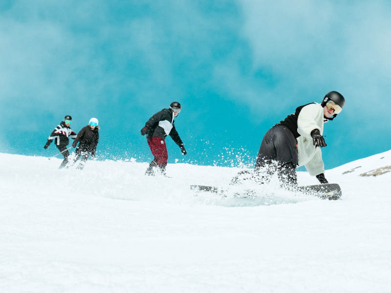 Image of group skiing down snowy mountain in the sunshine, fresh powder. One member of the group holds a lit flare.