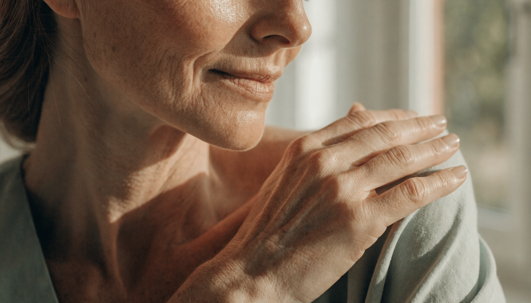 Vrouw legt rustig haar hand op haar schouder bij het raam