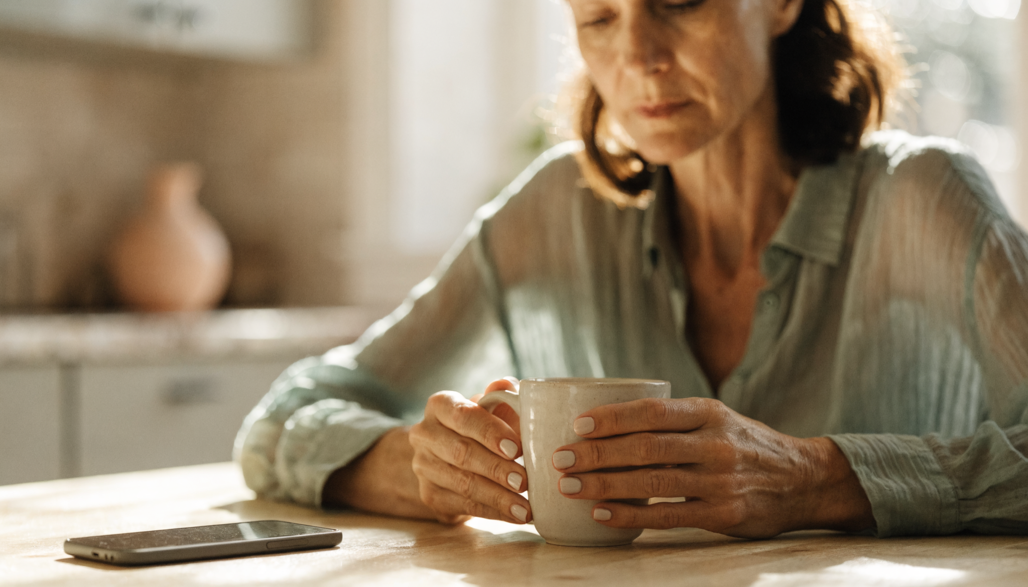 Vrouw aan de keukentafel met een mok en haar telefoon
