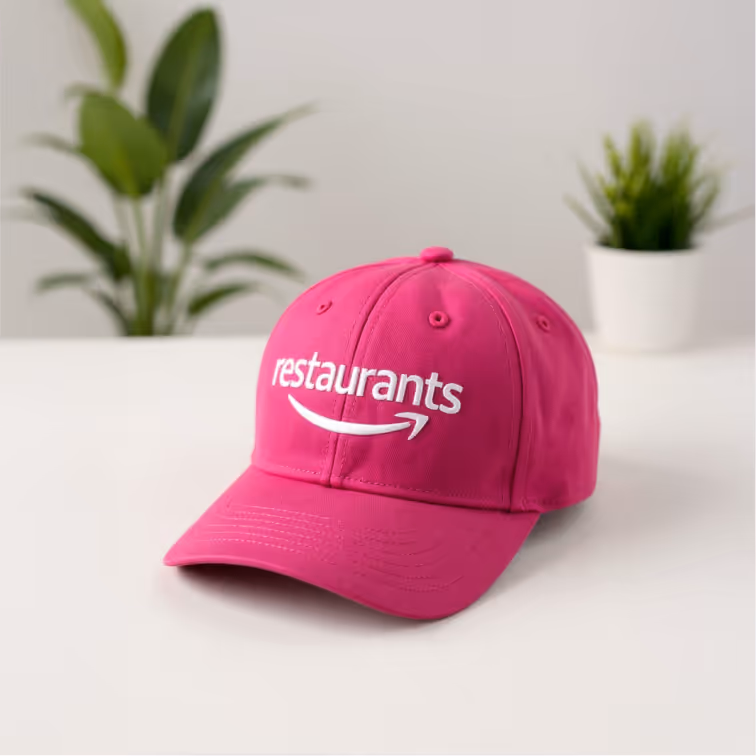 Magenta baseball cap with restaurants logo and plants in background.