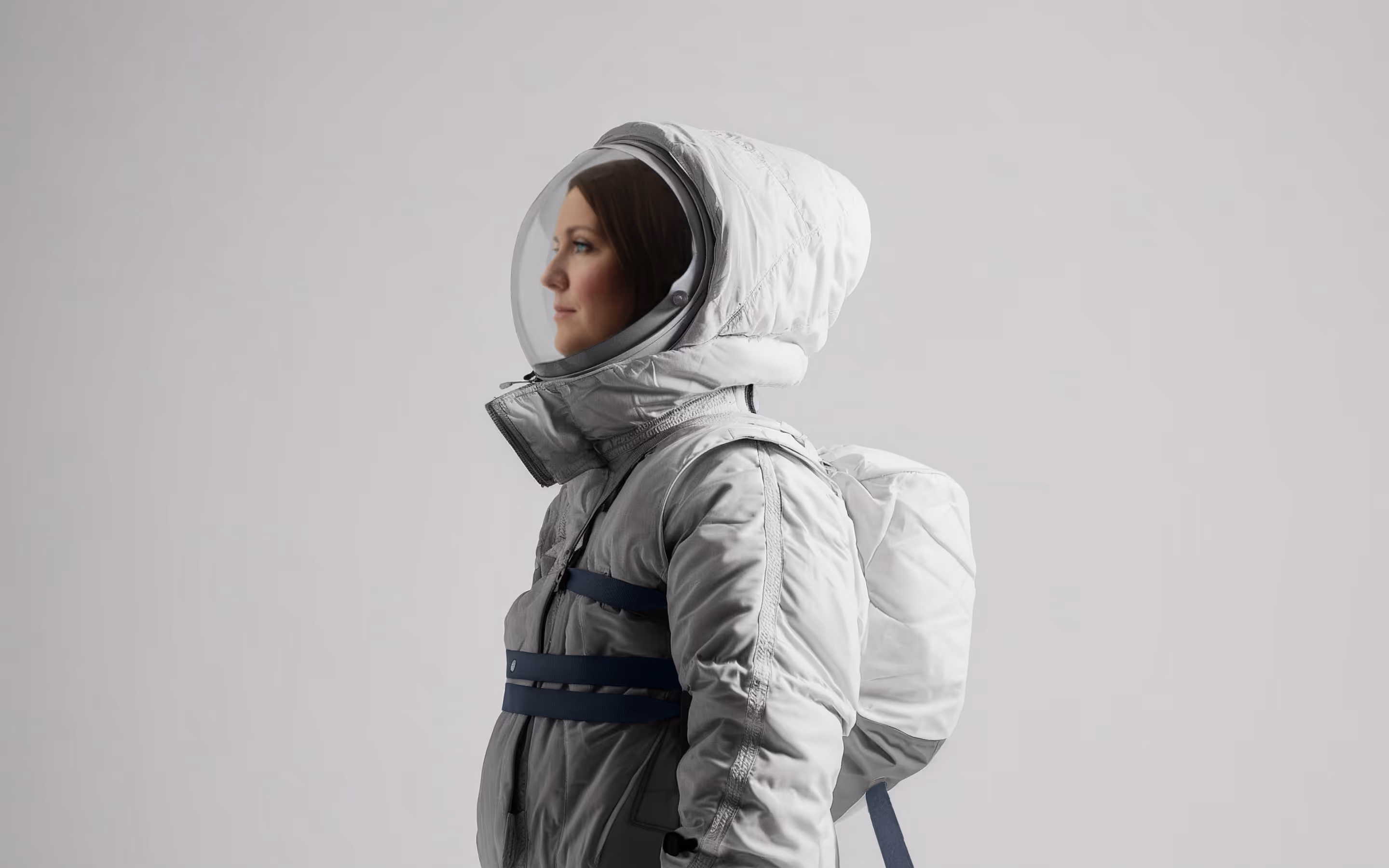 Katie Swanson in white spacesuit and helmet looking left against gray background.