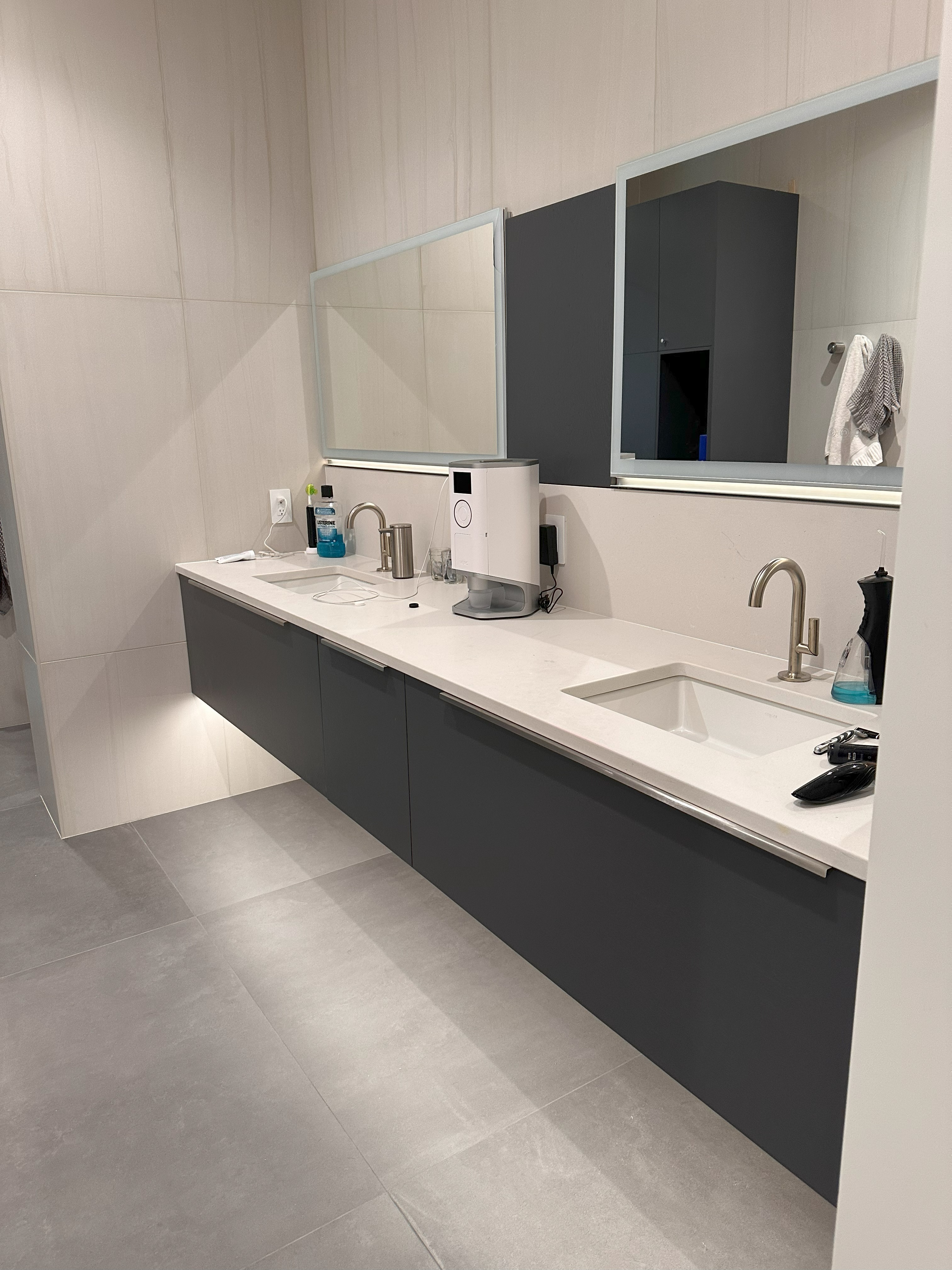 Modern bathroom with two rectangular sinks set in a light countertop with dark lower cabinets, two framed mirrors above, a soap dispenser, a bottle of mouthwash, a wall-mounted device, and a few grooming items on the countertop.