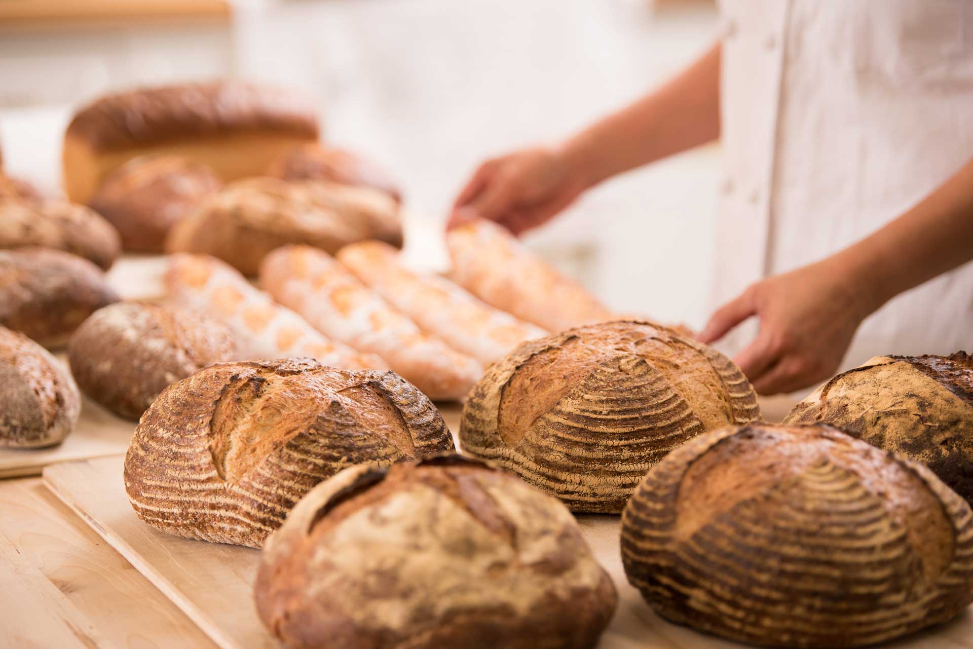 A woman is reaching for a loaf of bread on a table.