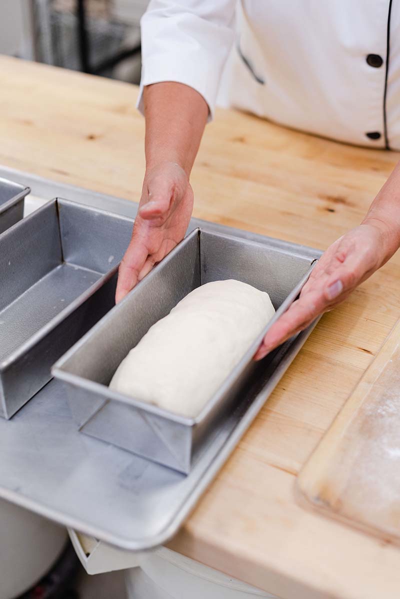 A person is holding a loaf of bread in a metal pan.
