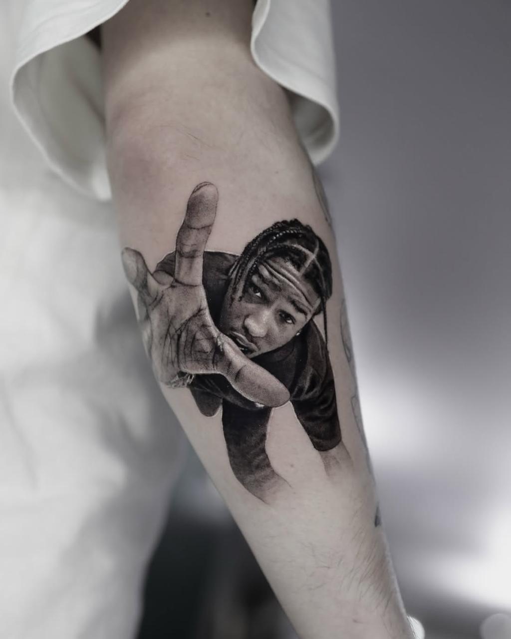 Tattoo-Künstler skizziert ein klassisches Gesichtsbild auf dem Unterarm einer Person, mit einer digitalen Referenz auf einem Tablet nebenan.