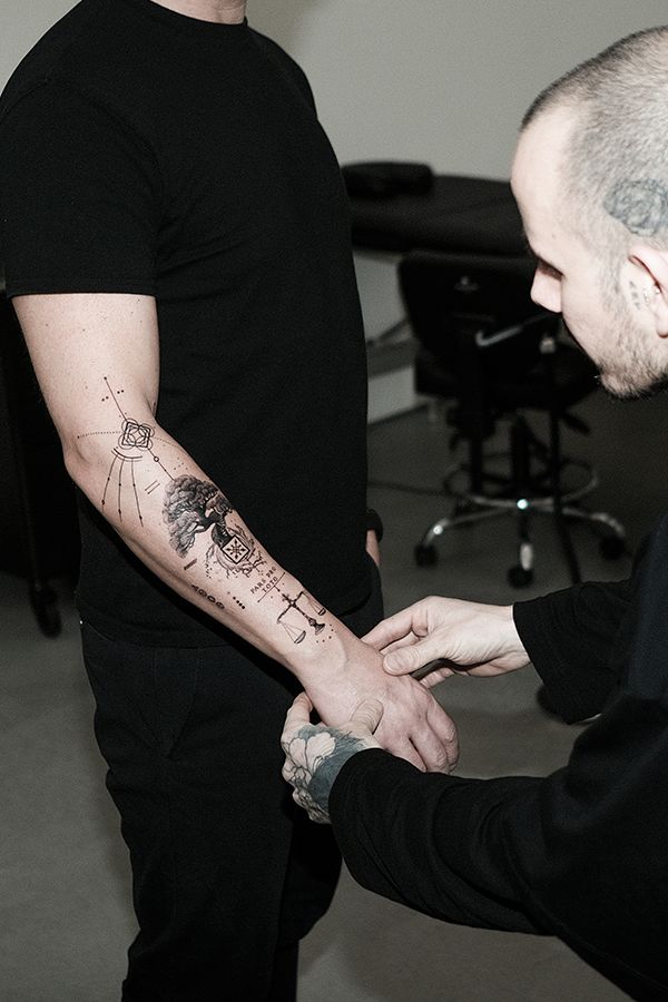 Eine Tätowiererin überprüft den Unterarm eines Mannes mit einem frischen schwarzen Tätowierungsdesign.