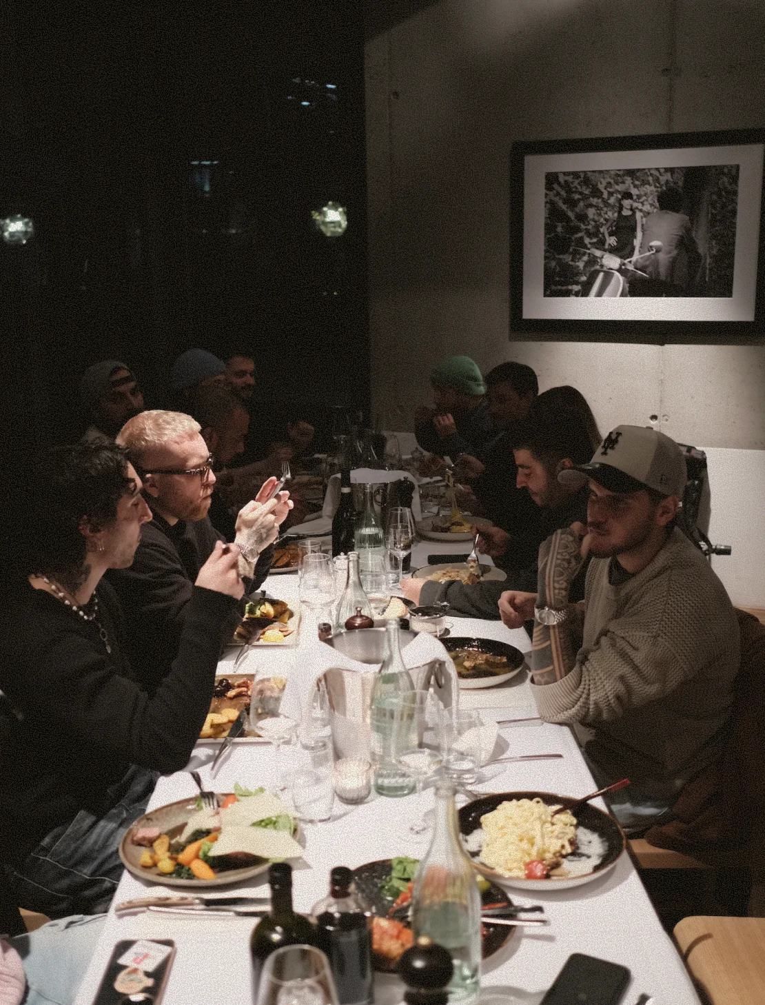 Gruppe junger Männer sitzt bei gedämpftem Licht an einem lang gedeckten Tisch und genießt ein gemeinsames Abendessen.