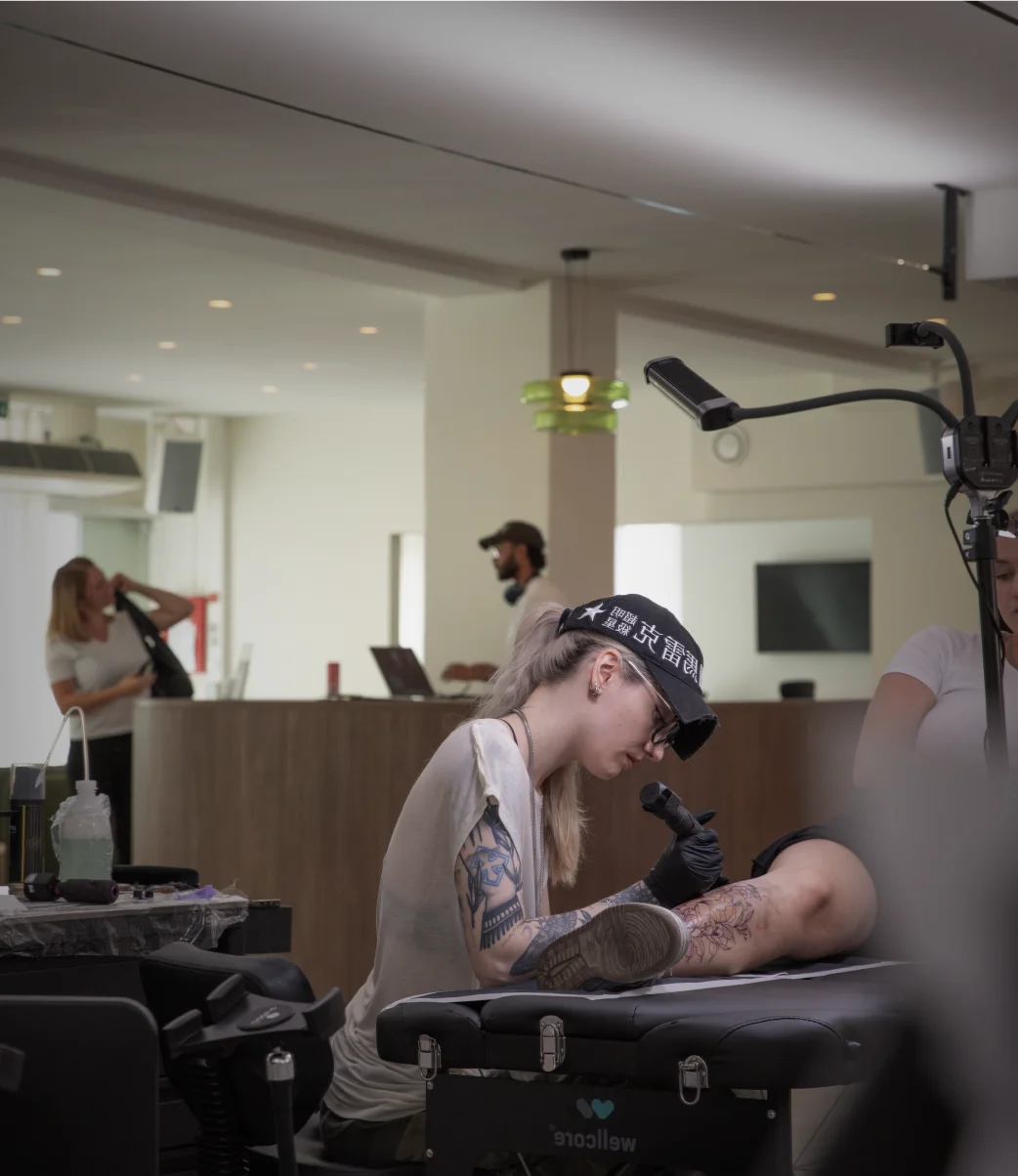 Tattoo-Künstlerin mit schwarzer Kappe tätowiert das Bein eines Kunden in einem modernen Studio.
