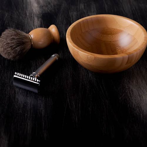 Traditional shaving set with razor, brush, and wooden bowl on dark surface