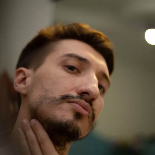 Man examining his patchy beard in the mirror, looking for natural growth solutions