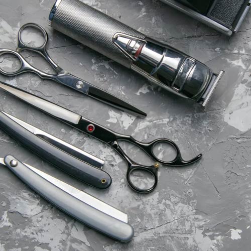 Barber tools including scissors, straight razors, and clippers on a textured surface