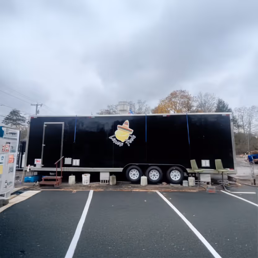 Black food truck with "Lemon Food" logo, parked in an empty lot under a cloudy sky.