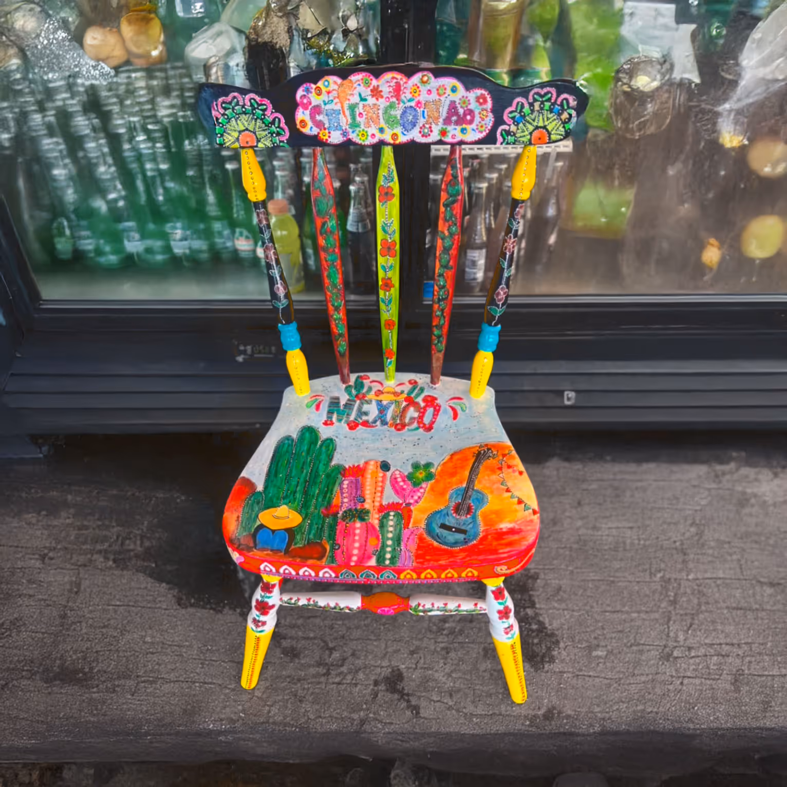 A colorful, hand-painted wooden chair with "Mexico" on the seat, featuring bright floral and cactus designs.
