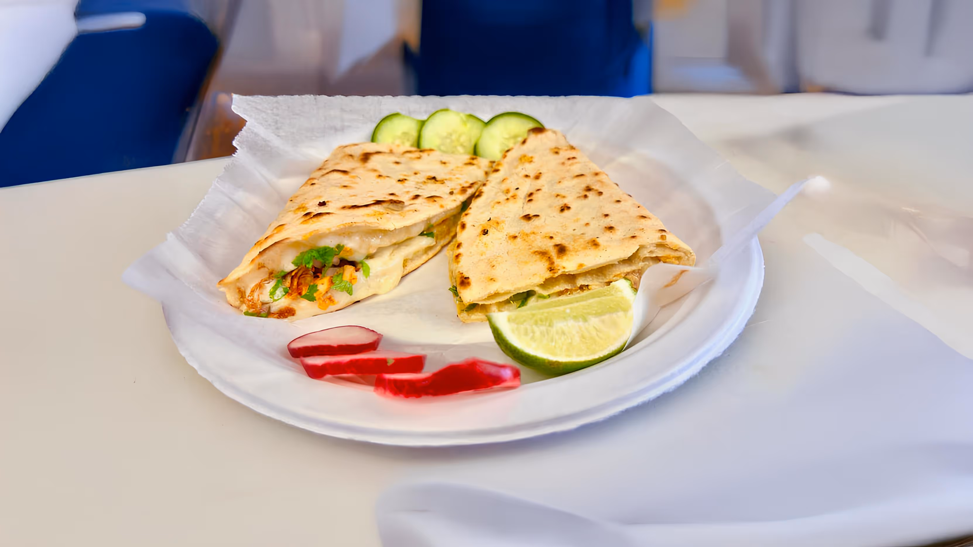 Quesadilla slices on a white plate. Cucumber slices, lime wedges, and radish strips are on the side.