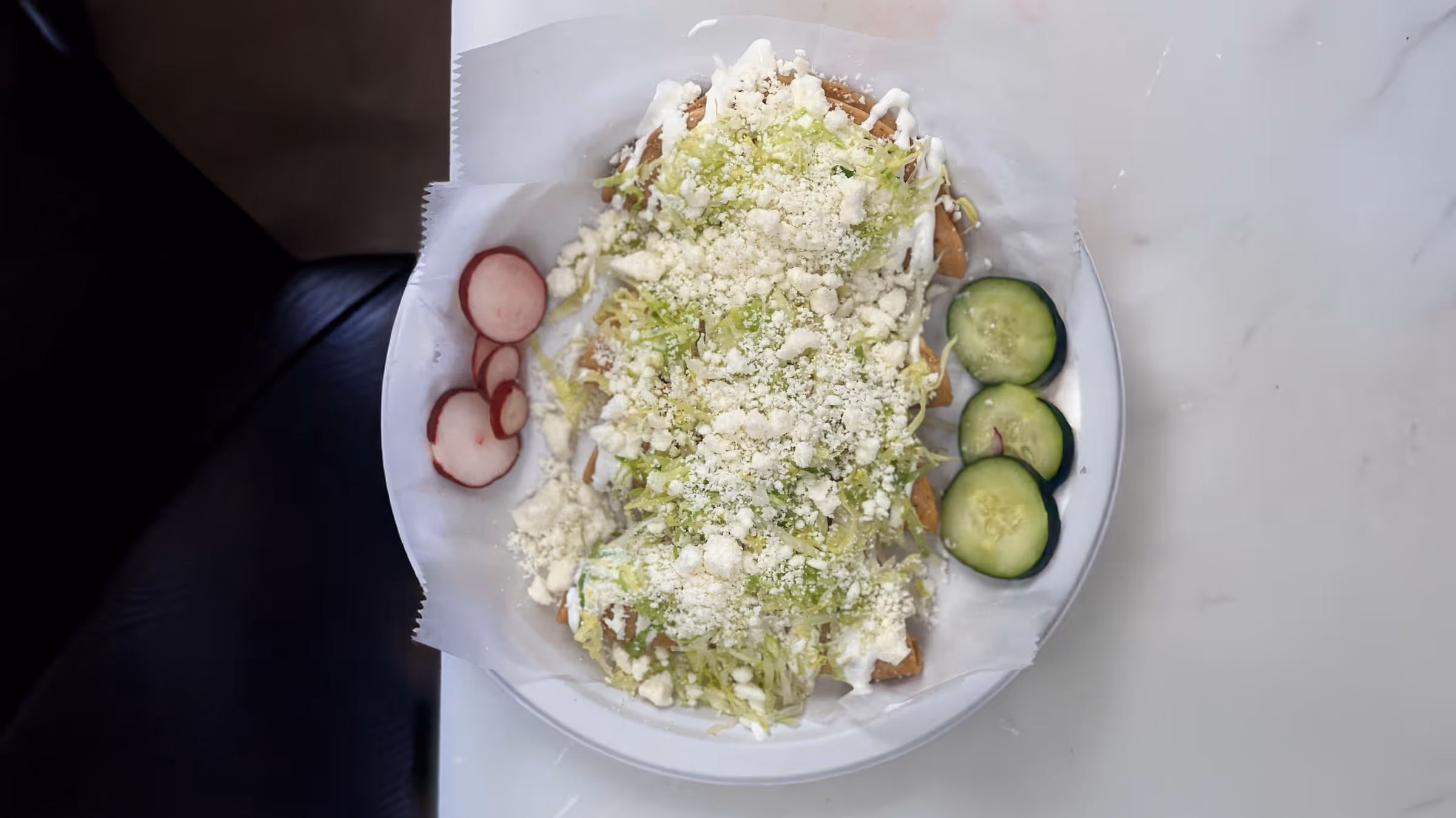 A plate of four Sopes topped with shredded lettuce, crumbled cheese, and cream; radish and cucumber slices on the side.