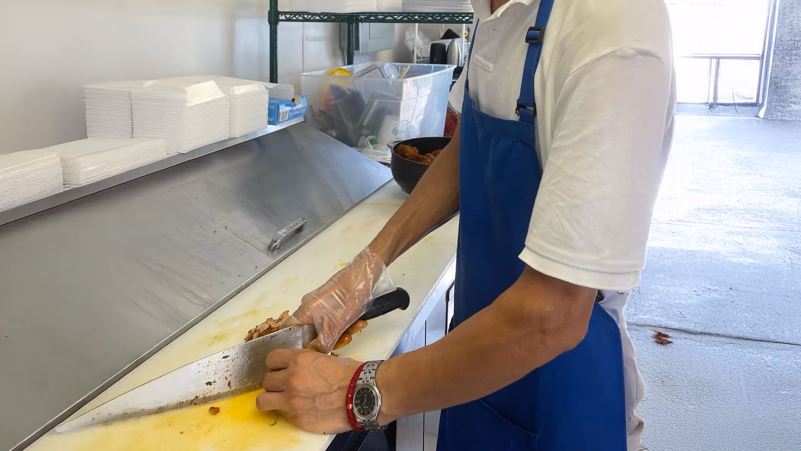 A person in a blue apron and white shirt slices food on a white cutting board.