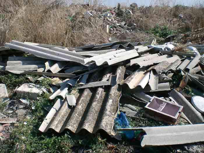 Dépôt sauvage de plaques de fibrociment amianté brisées abandonnées dans un terrain en friche, déchets de chantier illégalement déposés en pleine nature