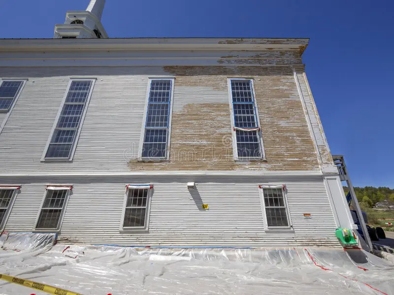 Façade d'un bâtiment ancien en cours de décapage de peinture au plomb, avec bâche de protection au sol et fenêtres masquées pour confiner les poussières