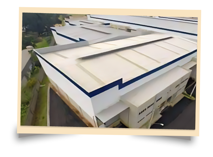 Foto aérea de um grande galpão industrial com teto branco e detalhes em azul escuro.