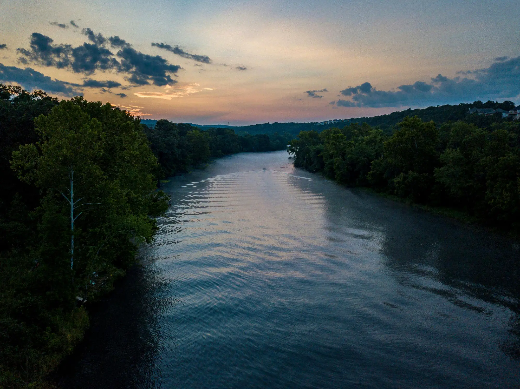 Serene Missouri river scene at dusk, with gentle ripples reflecting a colorful sky and lush greenery along the banks.