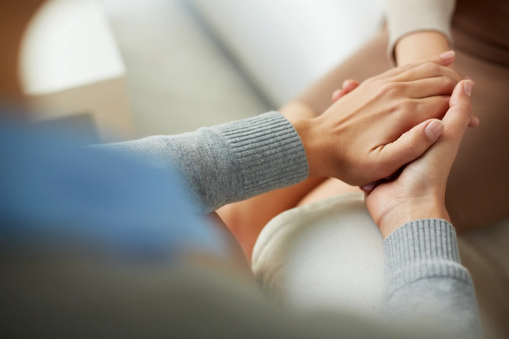 Two hands are clasped together, conveying a sense of support and comfort, with soft fabric textures visible in the background.