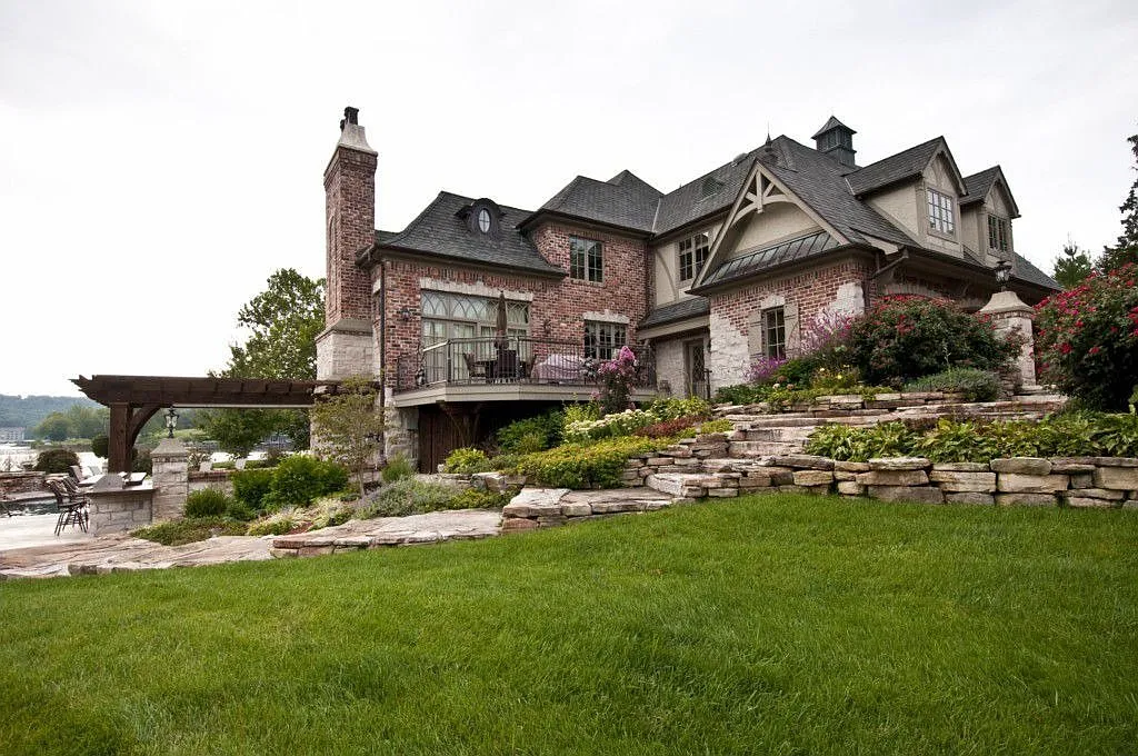 Elegant brick house featuring landscaped gardens, stone steps, and a patio overlooking a scenic view. Perfect for outdoor relaxation.