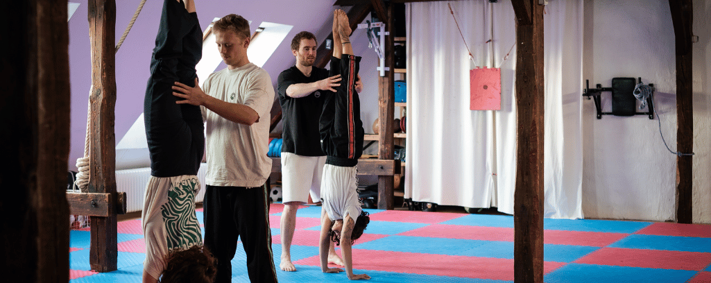 Gruppe übt eine Handstand-Partnerübung und erlebt Bewegung als sozialen Dialog voller Vertrauen und Kooperation.