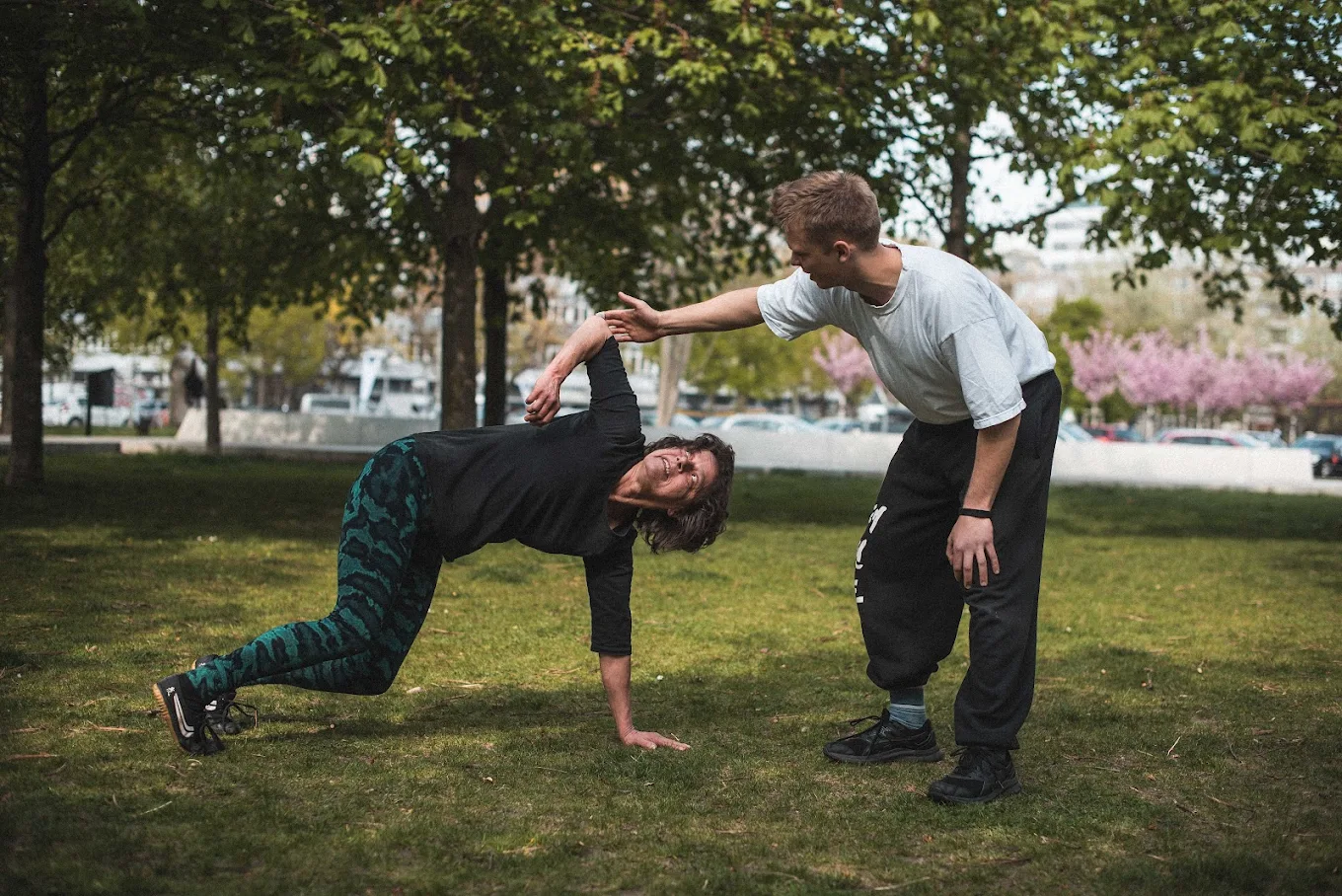 Zwei Personen trainieren gemeinsam im Park und erkunden durch Partnerübungen, wie Bewegung Verbindung schafft.