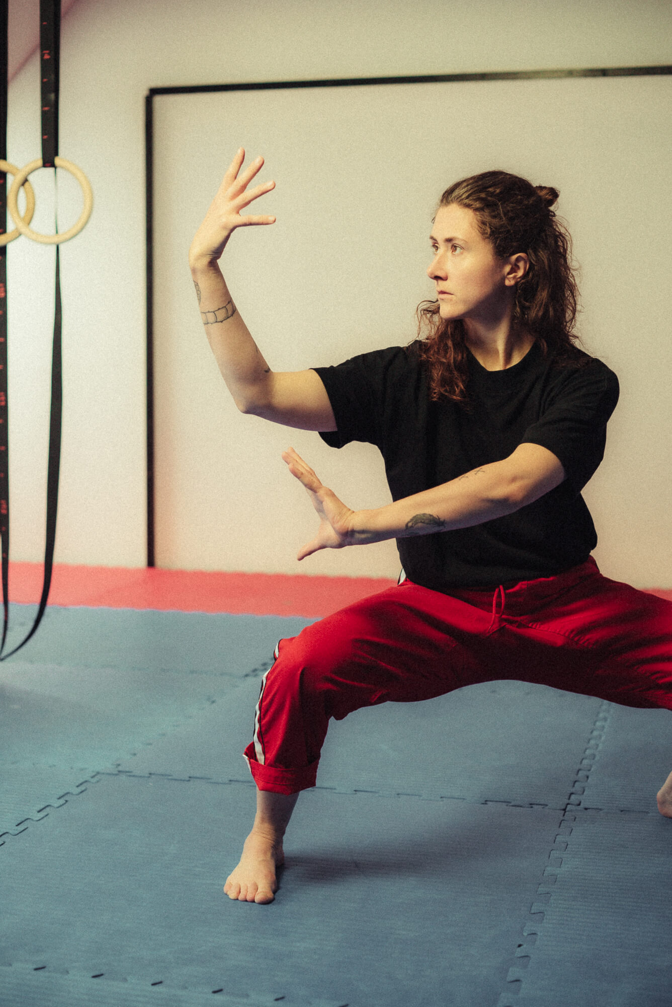 Kursleiterin Person Kampfkunst-Position mit erhobenen Armen auf Trainingsmatte – Fokus auf Körperhaltung und Bewegungskontrolle.