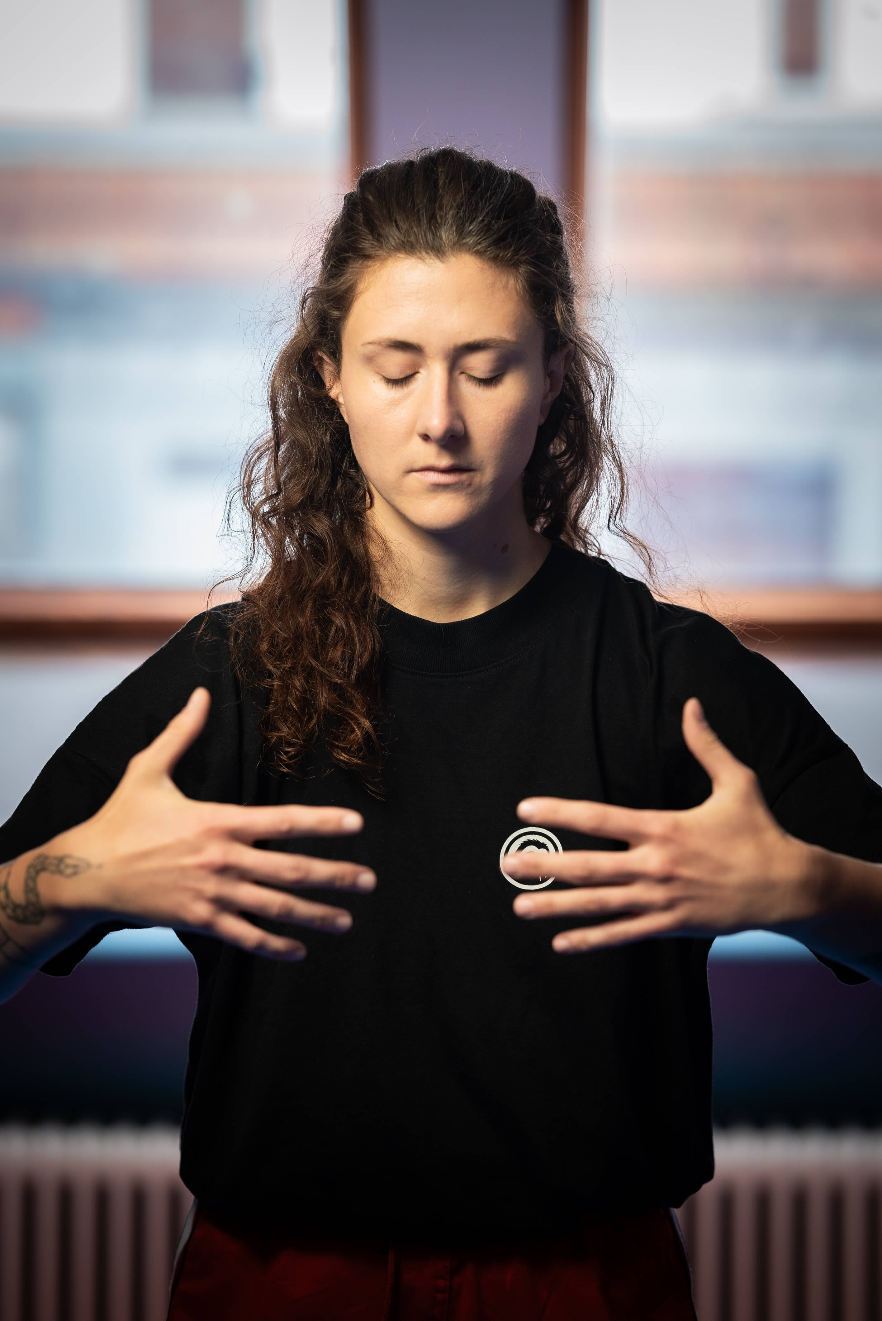 Trainerin steht mit geschlossenen Augen und gehobenen Händen in einer meditativen Qi-Gong-Haltung.