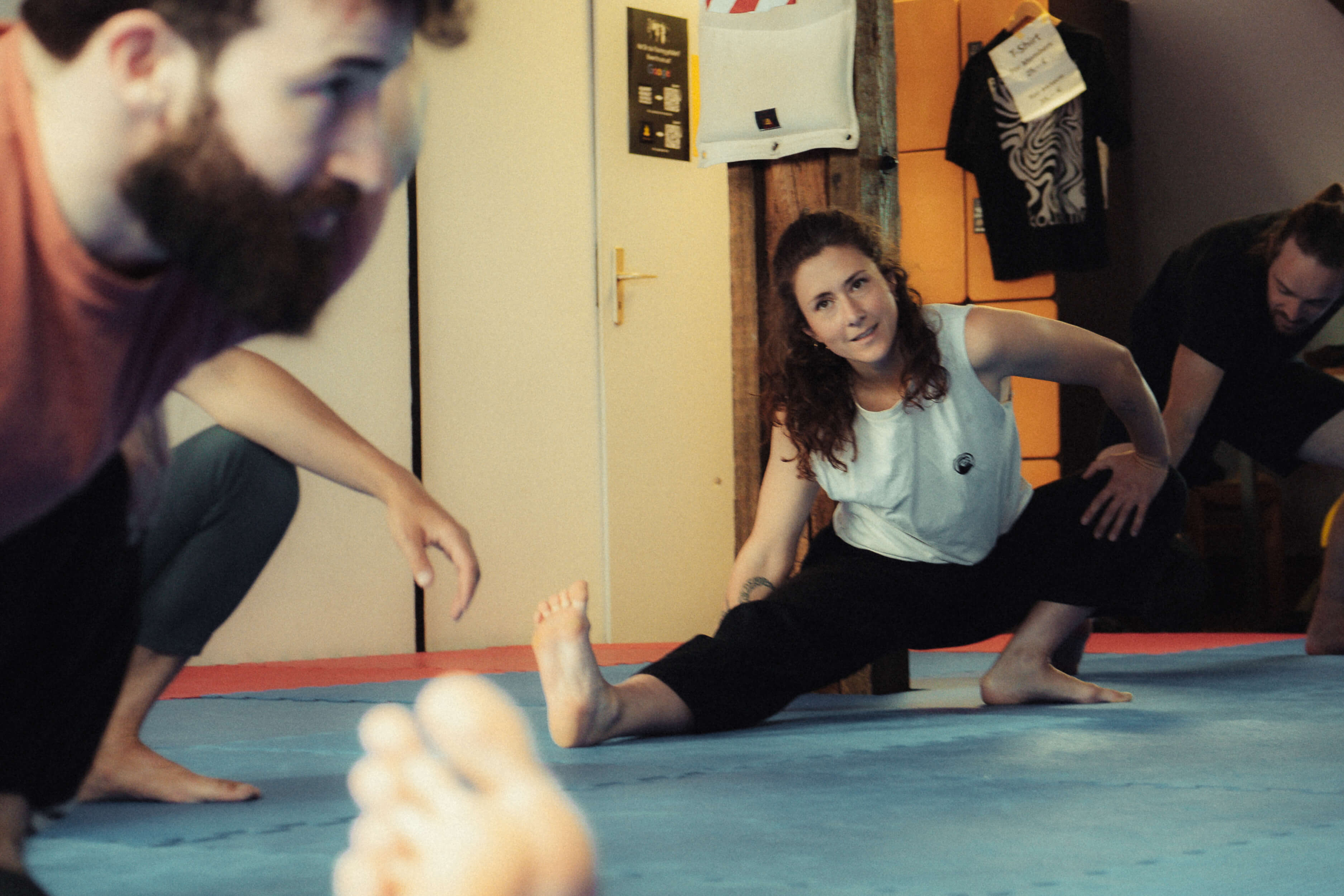 Trainerin leitet Teilnehmende bei einer Dehnübung auf der Matte an.