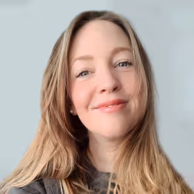 Smiling woman with long light brown hair and light blue eyes against a pale gray background.