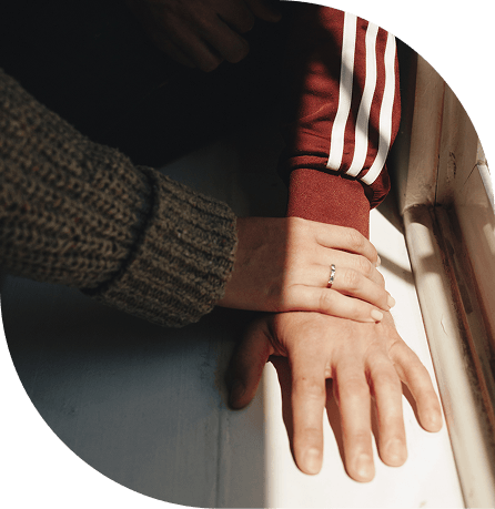 Two hands touching on a windowsill, one wearing a ring and the other in a red sleeve with white stripes.