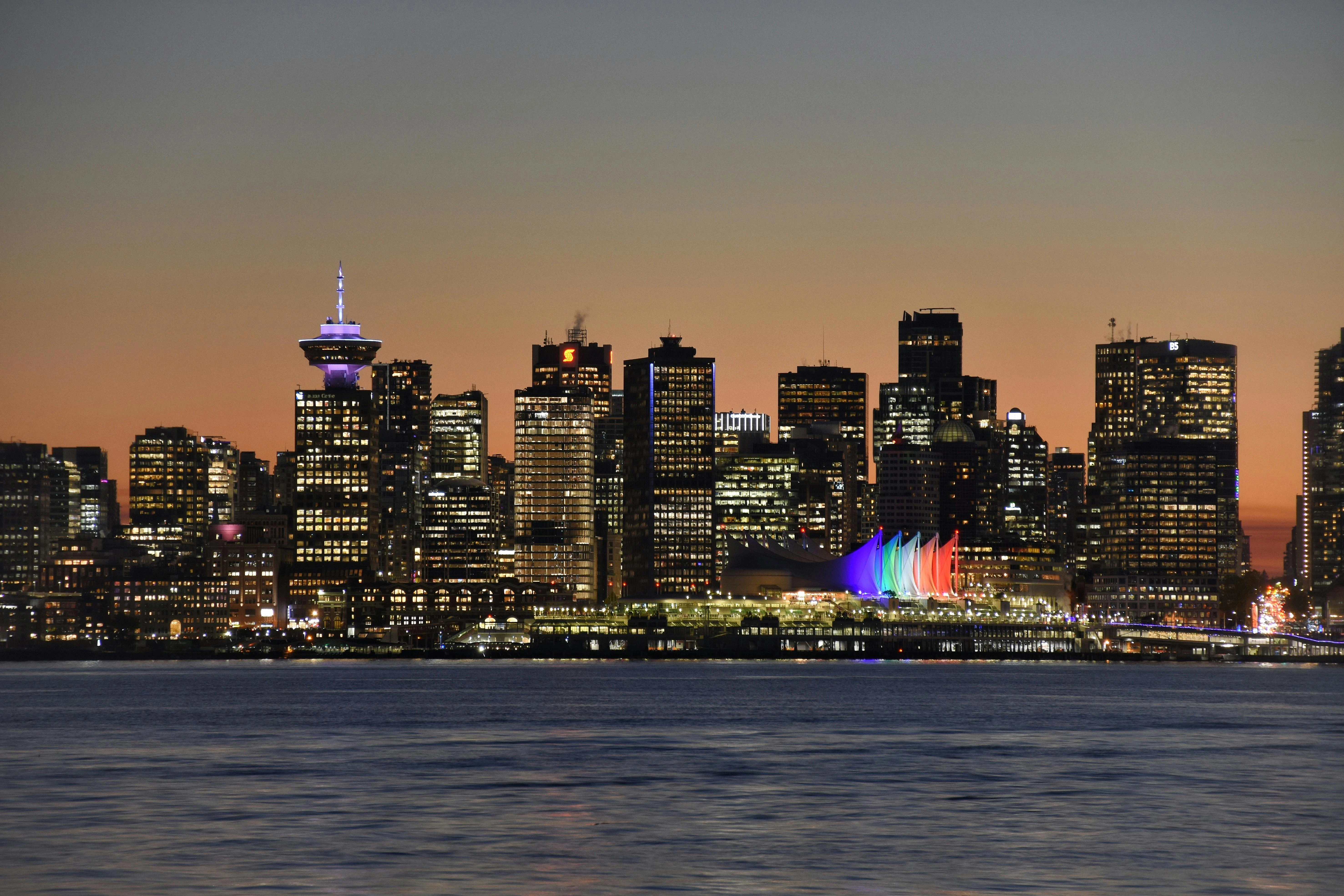 Panoramic view of the Vancouver skyline at sunset featuring the colorful sails of Canada Place across the Burrard Inlet.
