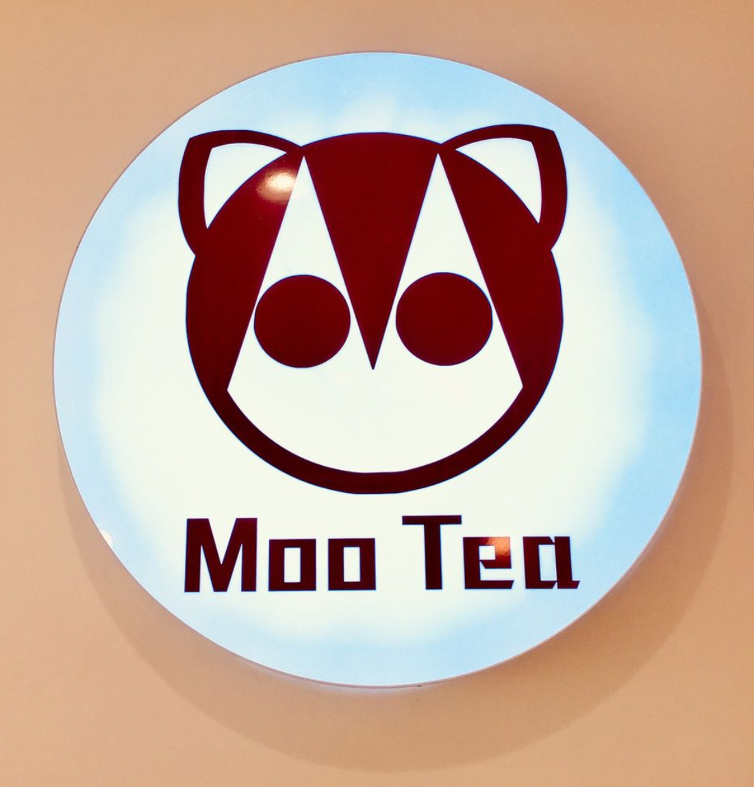Circular lighted sign with stylized red animal face and text 'Moo Tea' underneath.
