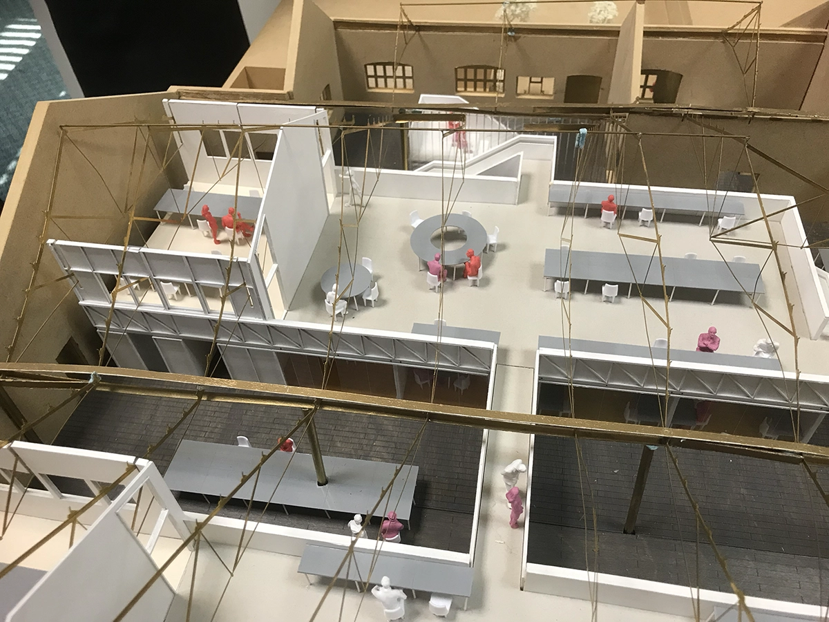 Architectural model of an office space showing desks, seating areas, and miniature colored human figures under a geometric ceiling framework.