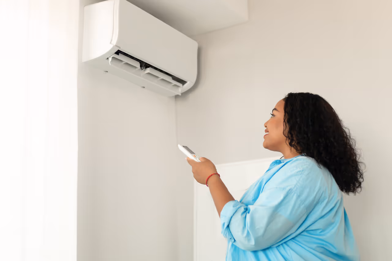 A woman in a blue blouse uses a remote to control a wall-mounted air conditioner. 