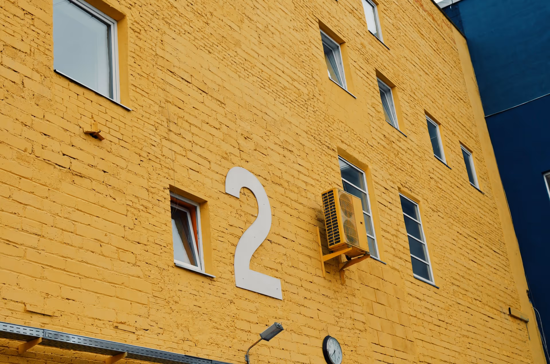 Yellow brick building with multiple windows, large white number 2, and an air conditioning unit. 