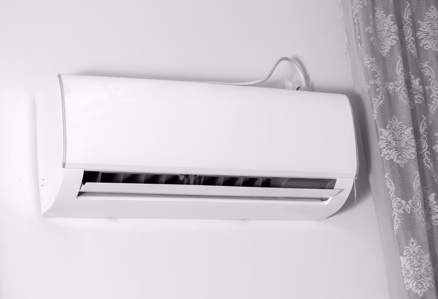 Wall-mounted white air conditioner running, with a patterned curtain partially visible to the right. 