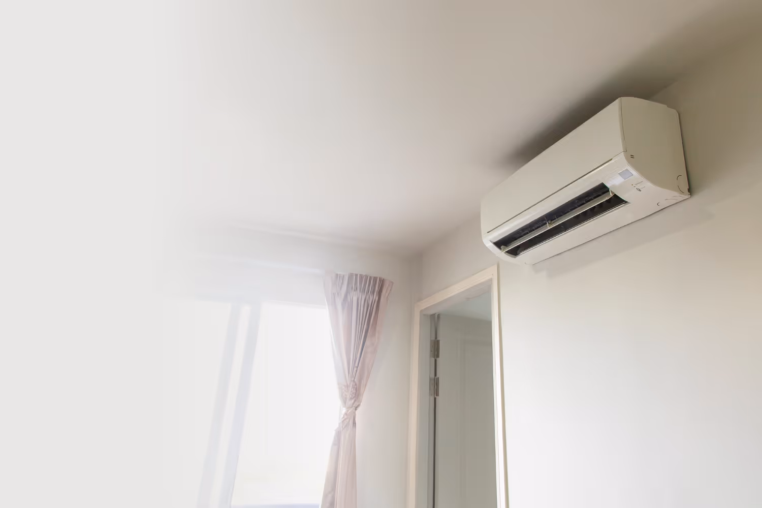 Wall-mounted air conditioner above a door in a bright, minimalistic room. 