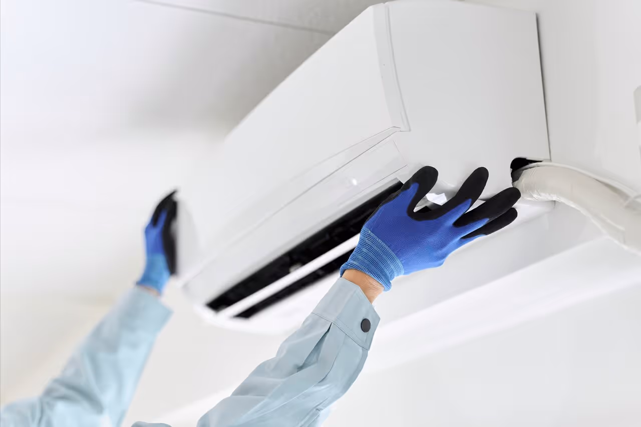 A technician in blue gloves adjusts a white wall-mounted air conditioning unit. 