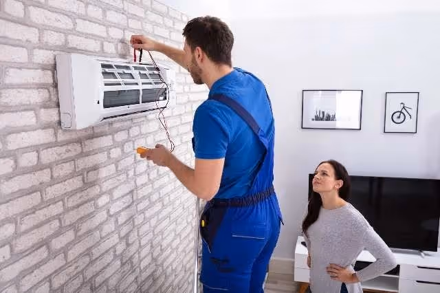 Technician repairs AC unit while woman watches.