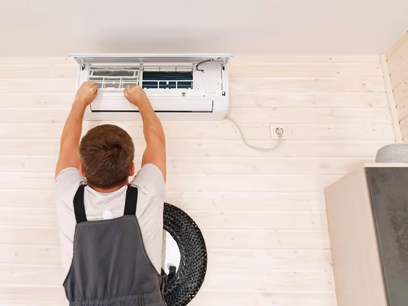Technician works on AC unit filter overhead.