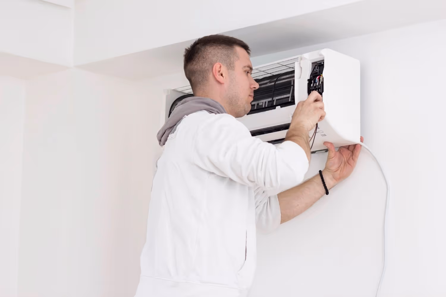 Man repairs internal wiring of wall AC.