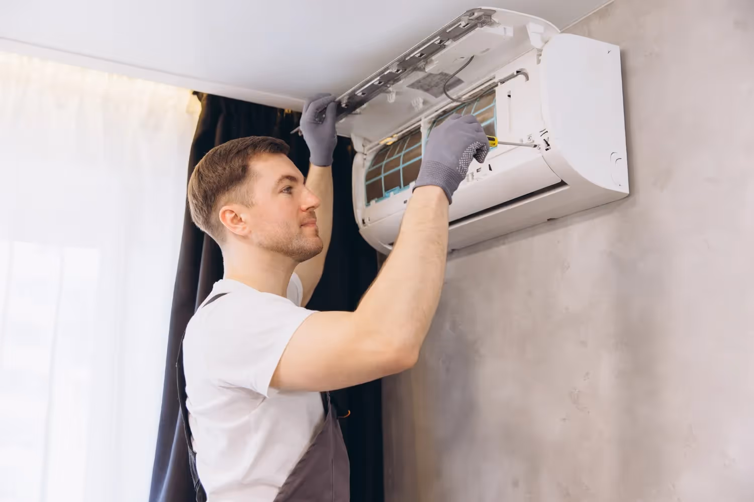 Man in gloves services wall-mounted AC unit.