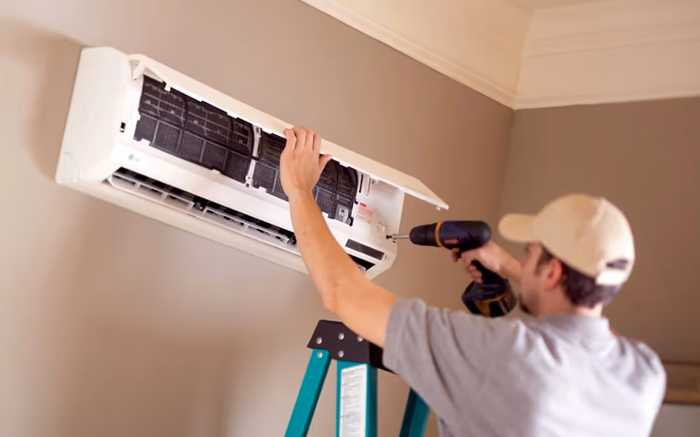 Man installing indoor mini-split unit with drill.